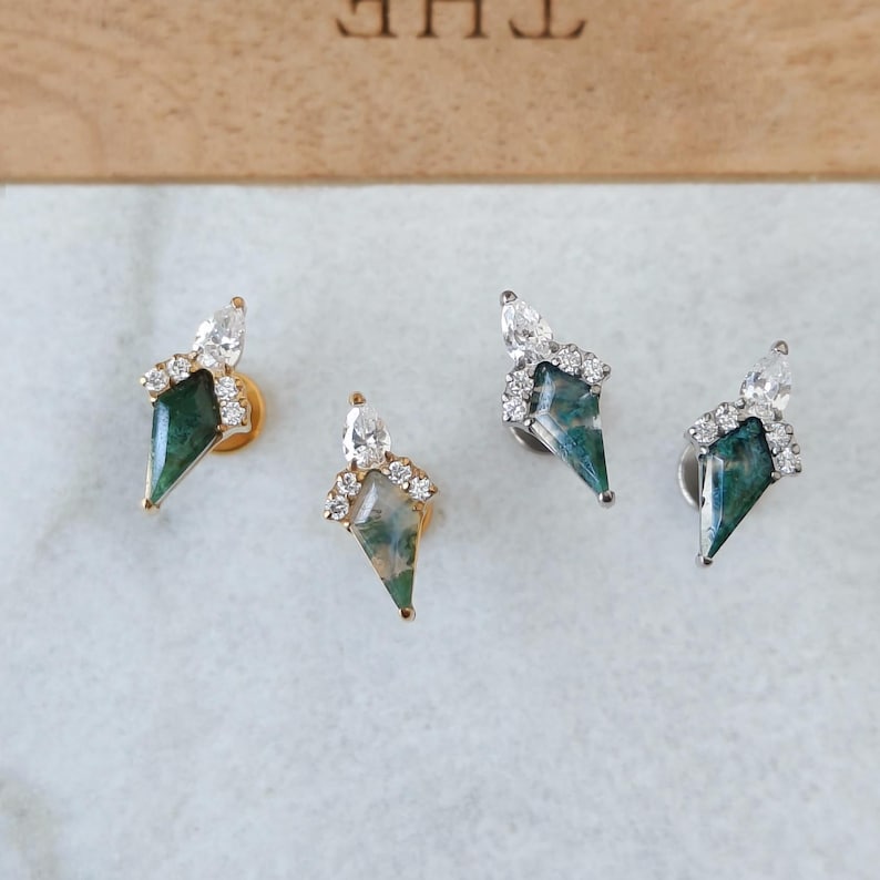 May include: Four gemstone stud earrings. Each earring features a green and white gemstone in a kite shape, topped with a cluster of small clear stones and a larger clear stone. Two earrings have gold posts, and two have silver posts.