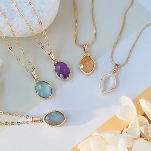 May include: Five gold necklaces with different colored gemstone pendants. The pendants are all oval shaped and have a gold setting. The gemstones are amethyst, aquamarine, moonstone, labradorite, and citrine.