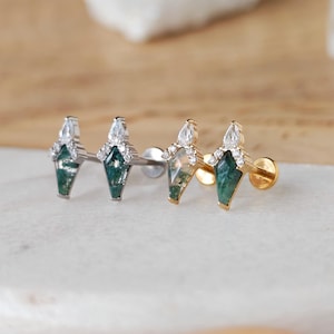 May include: Close-up of three stud earrings. Each earring features a green gemstone in a geometric shape, accented with clear crystals and a pear-shaped stone at the top. The earrings are set in silver and gold tones.