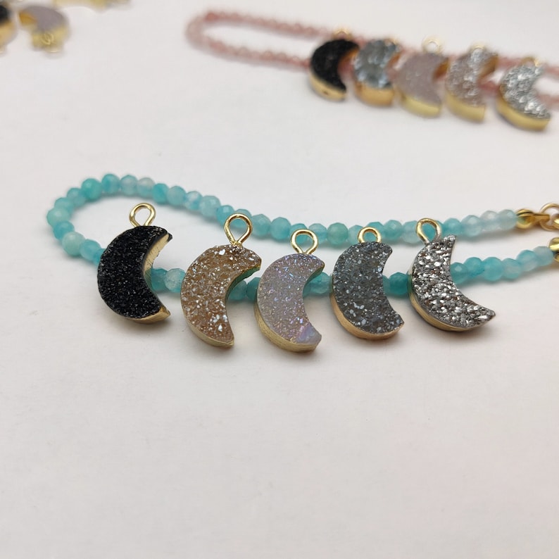 May include: A turquoise beaded bracelet with six crescent moon charms. The charms are made of different types of agate, including black, brown, white, and grey.
