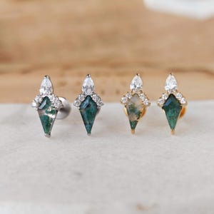 May include: Four gemstone earrings. Two earrings have silver posts, and two have gold posts. Each earring features a teardrop-shaped green stone with white accents, a pear-shaped clear stone, and small clear stones.