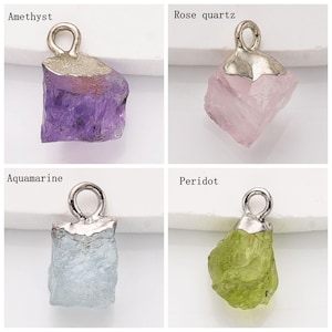May include: Four silver charm pendants with different colored gemstones. The gemstones are amethyst, rose quartz, aquamarine, and peridot.