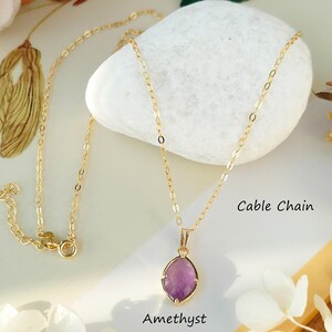 May include: A gold cable chain necklace with a purple amethyst pendant. The necklace is on a white rock with the text "Cable Chain" and "Amethyst" below it.