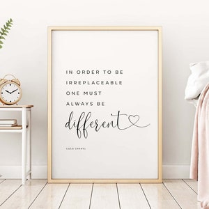 May include: A black and white inspirational quote print with a gold frame. The quote reads "In order to be irreplaceable one must always be different."  The quote is attributed to Coco Chanel.