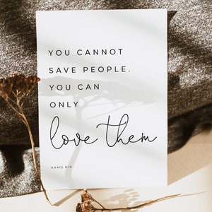 May include: A white rectangular print with the quote "You cannot save people. You can only love them" by Anais Nin in black text. A dried flower stem is in the foreground.