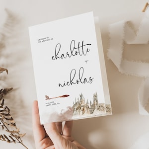 Puede incluir: Una invitación de boda blanca con el texto "Welcome to the Wedding of Charlotte + Nicholas". La invitación presenta una ilustración en acuarela de un castillo, una escoba y un búho. La fecha y el lugar también están impresos.