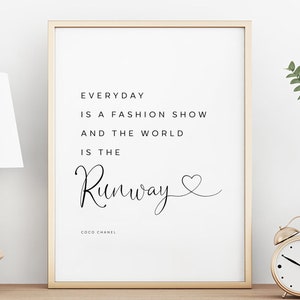 Może przedstawiać: Oprawiony wydruk z cytatem "Everyday is a fashion show and the world is the Runway" Coco Chanel. Czarny tekst na białym tle, oprawiony w złoto. Złoty budzik i biała lampa są widoczne.