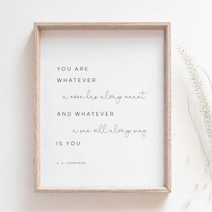 Puede incluir: Impresión enmarcada con fondo blanco y texto negro. El texto dice "YOU ARE WHATEVER a moon has always meant AND WHATEVER a sun will always sing IS YOU" de E. E. Cummings. El marco es de color marrón claro.
