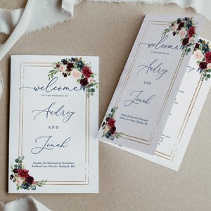 Puede incluir: Tarjetas de bienvenida de boda con arreglos florales en tonos burdeos, azul marino y rubor. Las tarjetas presentan marcos dorados y una escritura elegante, dando la bienvenida a Audrey y Jonah a su boda. La fecha y el lugar también están impresos.