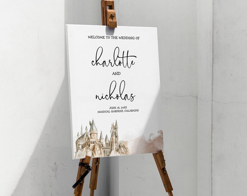 May include: A white wedding welcome sign on a wooden easel. The sign reads "Welcome to the Wedding of Charlotte and Nicholas" with the date and location below. A watercolor image of a castle is at the bottom.