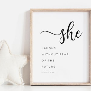 May include: A framed print with a white background and black text that reads "She laughs without fear of the future, Proverbs 31:25".