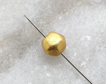 May include: A gold-colored metal bead with a faceted, irregular shape. The bead is threaded on a thin, silver-colored wire.