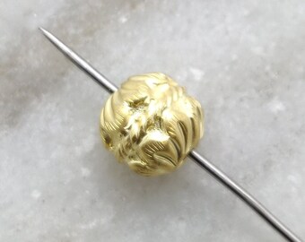 May include: A gold-colored bead with a textured, floral design. The bead is threaded on a thin, silver-colored wire.
