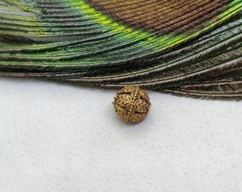 May include: A gold-colored metal bead with a decorative, intricate design. The bead is round and has a textured surface.