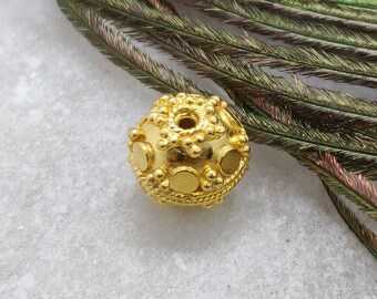 May include: A gold bead with a textured surface and a circular hole in the center. The bead is surrounded by a peacock feather.