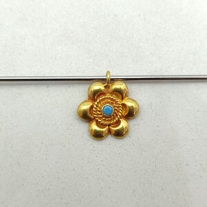 May include: A gold flower pendant with a blue gemstone in the center. The pendant has a detailed design with a rope-like border around the gemstone.