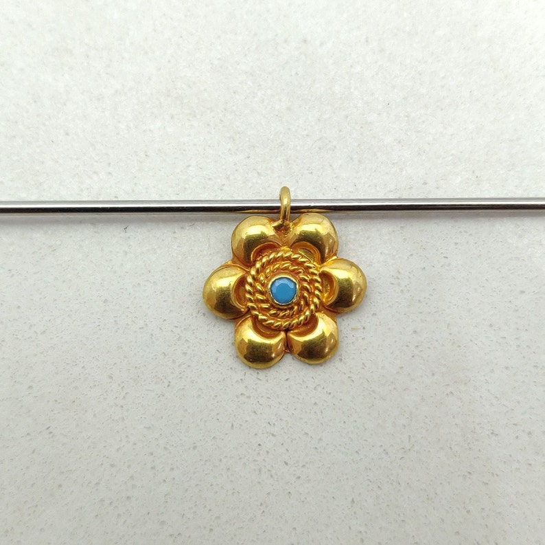 May include: A gold flower pendant with a blue gemstone in the center. The pendant has a detailed design with a rope-like border around the gemstone.