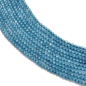 Può includere: Una collana di perline di pietra preziosa sfaccettata blu chiaro. Le perline sono rotonde e hanno una superficie leggermente strutturata.