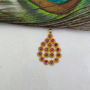 May include: A gold pendant with a teardrop shape, featuring a cluster of small, round, ruby-red stones set in gold.