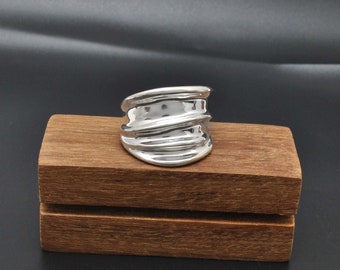Può includere: Un anello d'argento con un design ondulato e organico. L'anello è largo e ha una finitura liscia e lucida.