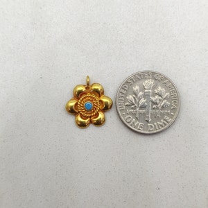 May include: Gold flower charm with a blue center stone. The charm is about the size of a dime.