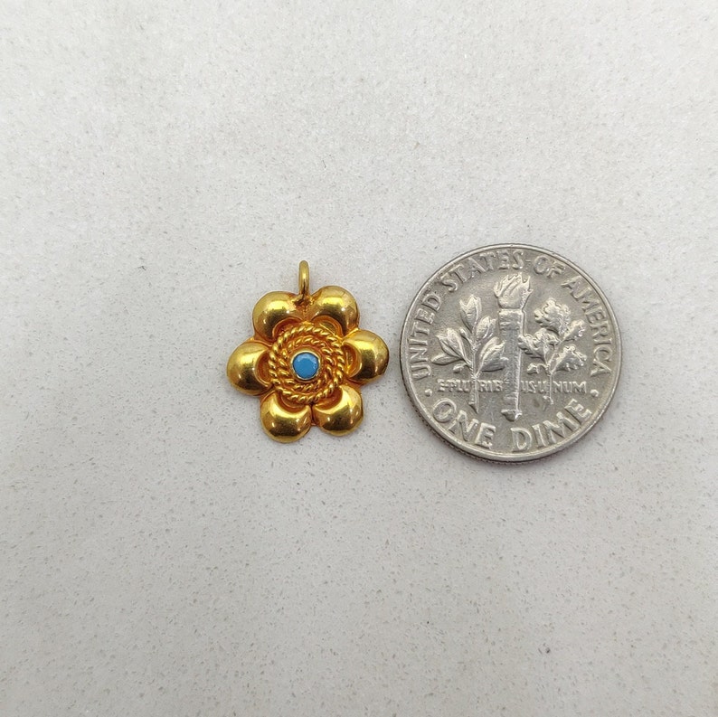 May include: Gold flower charm with a blue center stone. The charm is about the size of a dime.