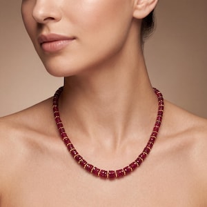 May include: A necklace featuring a series of faceted, deep red, cylindrical ruby beads arranged in a single strand. Each ruby bead is separated by a small, round, polished gold spacer bead, creating a consistent pattern along the entire length.