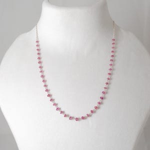 May include: A delicate silver chain necklace with small pink gemstones. The necklace is approximately 18 inches long.