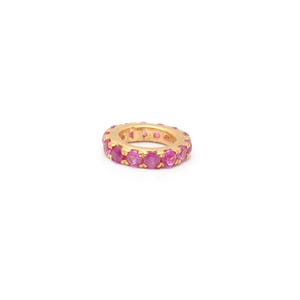 May include: A circular gold charm or ring featuring a continuous row of small, round, faceted pink gemstones set around the entire outer edge. The metal band has a polished yellow gold finish, and the stones are set in a prong-style setting.