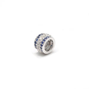 May include: A silver-toned ring with three rows of gemstones. The top and bottom rows feature small, deep blue stones, while the middle row has clear, sparkling stones. The ring is set against a white background.