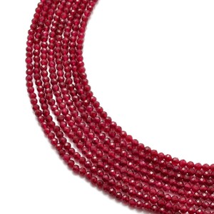 May include: A strand of red faceted gemstone beads. The beads are small and round, and they are strung together on a clear thread. The beads are arranged in a loose, flowing pattern.