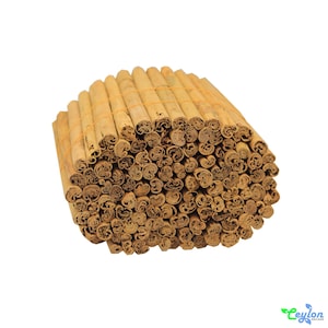 May include: A close-up of a bundle of cinnamon sticks, tied together with rubber bands. The sticks are a light brown color and have a rough texture.