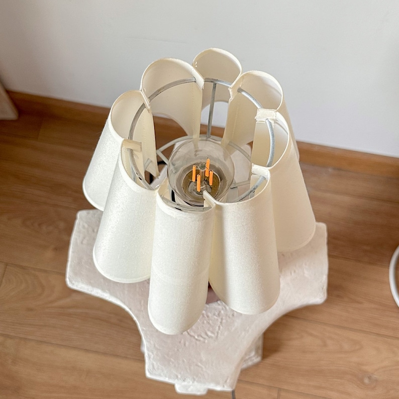 May include: A white lamp with a unique, ruffled lampshade. The lampshade is made of fabric and has a metal frame. The lamp is on a white base.