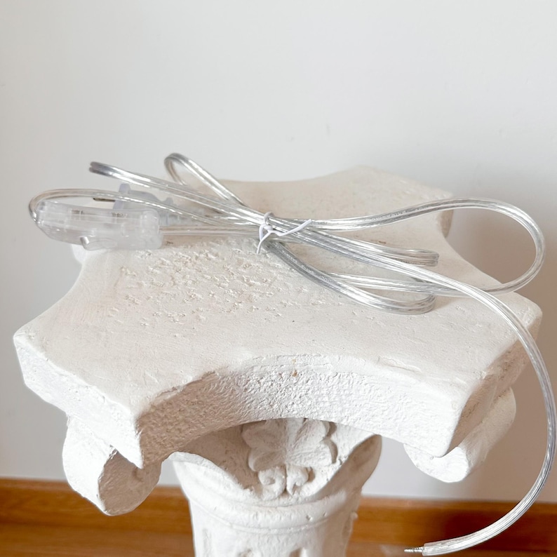 May include: A white pedestal table with a clear cord and plug. The cord is coiled on top of the table.