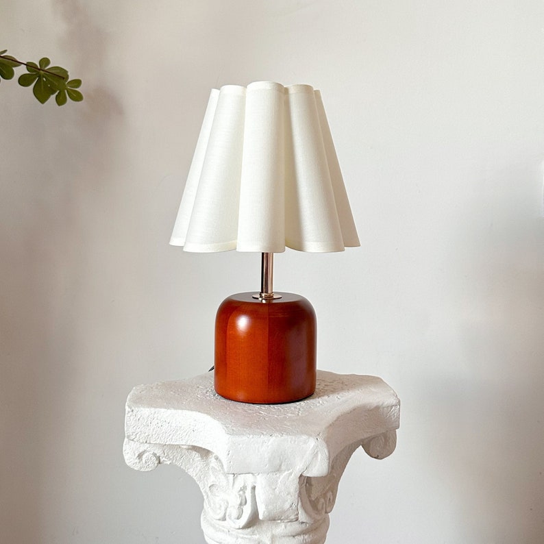 May include: A wooden table lamp with a white pleated lampshade. The lamp base is a dark brown cylinder shape.