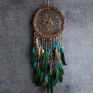 May include: A brown dreamcatcher with a green and gold beaded fringe and feathers. The dreamcatcher has a circular woven net with green and purple beads.
