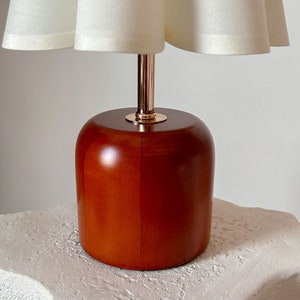 May include: A wooden table lamp with a white fabric lampshade. The lamp base is a rich brown color and has a gold metal accent.