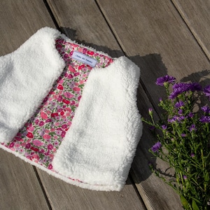 May include: White fleece vest with a pink floral lining. The vest has a small label that says "Older Sister" on it.