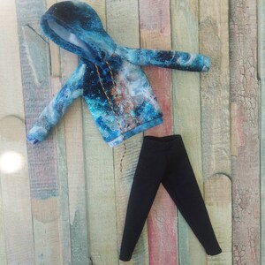 Puede incluir: Una sudadera con capucha de color azul y blanco con estampado de galaxia, cord&oacute;n de ajuste negro y pantal&oacute;n negro.