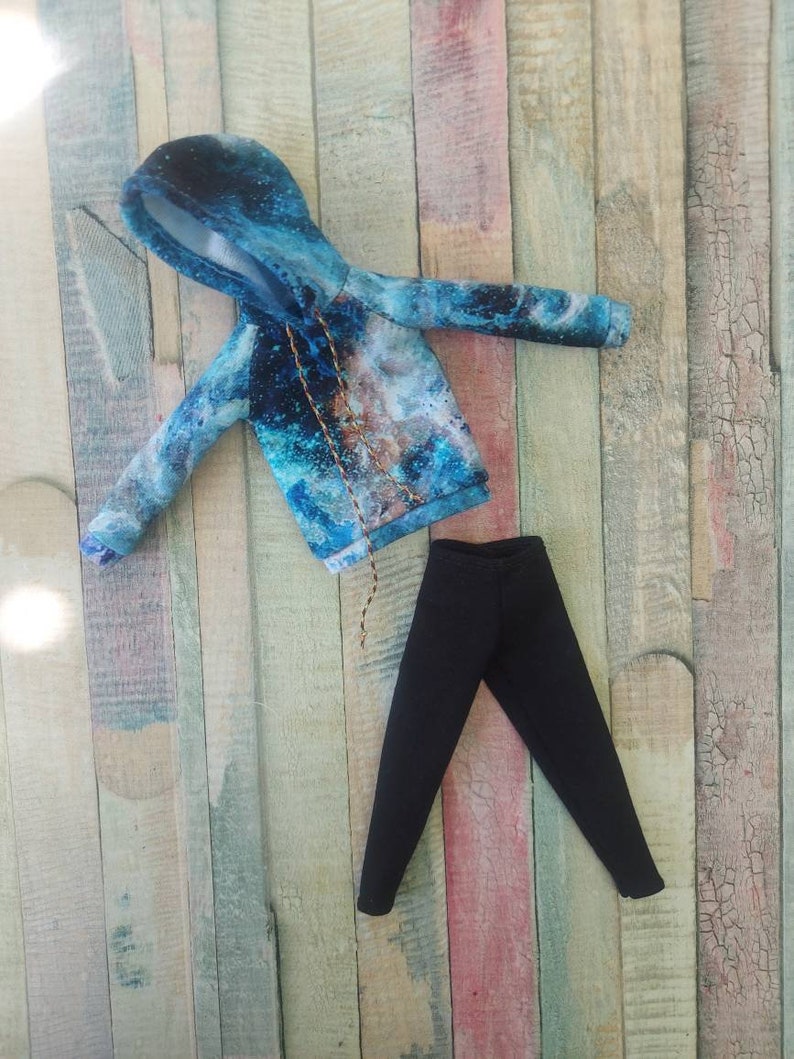 Puede incluir: Una sudadera con capucha de color azul y blanco con estampado de galaxia, cord&oacute;n de ajuste negro y pantal&oacute;n negro.