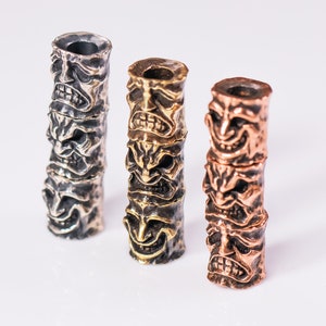 May include: Three stacked metal beads with a face design. The beads are silver, brass, and copper.