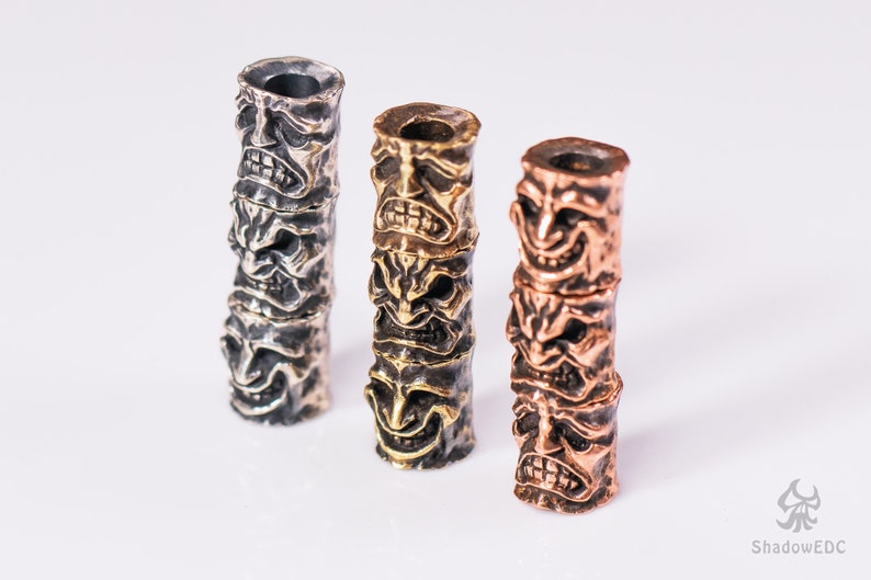 May include: Three stacked metal beads with a face design. The beads are silver, brass, and copper.