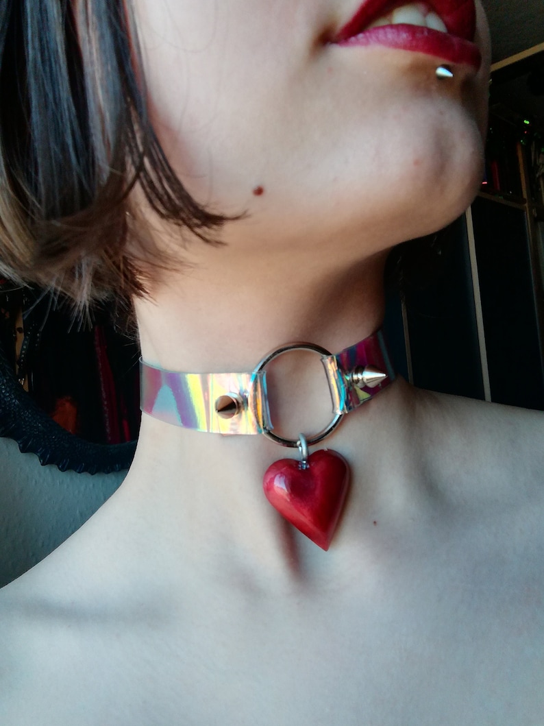 May include: A clear iridescent choker with a silver ring and a red heart pendant.