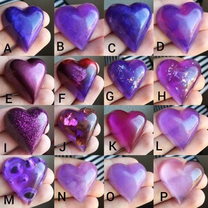 May include: Assortment of 16 heart-shaped resin crafts in various shades of purple, pink, and glitter. The hearts are arranged in four rows of four, with each heart having a letter label from A to P.