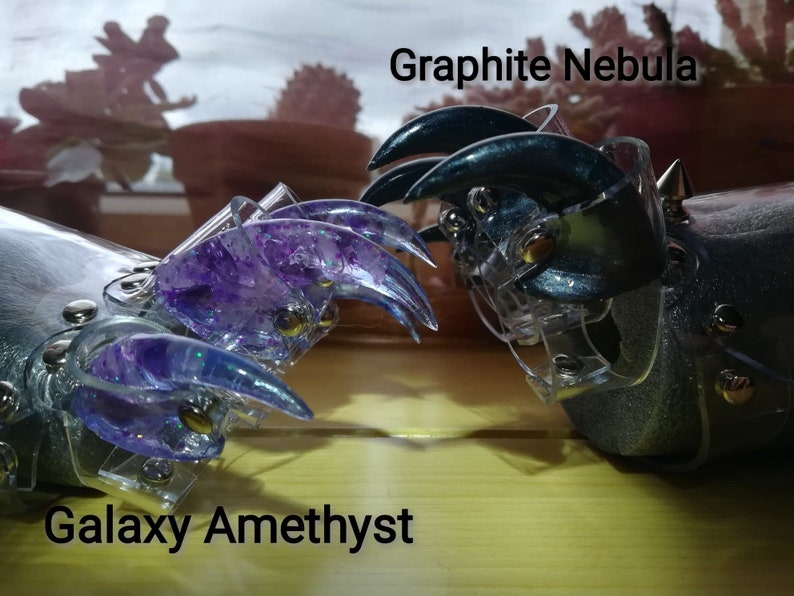 Puede incluir: Dos anillos en forma de garra con bases de pl&aacute;stico transparente. Un anillo est&aacute; decorado con purpurina morada y la etiqueta "Galaxy Amethyst". El otro anillo est&aacute; decorado con purpurina azul oscuro y la etiqueta "Graphite Nebula".
