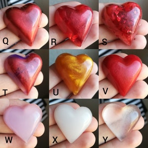 May include: Nine heart-shaped resin ornaments in various colours, including red, gold, pink, and white. Some have a glittery finish.