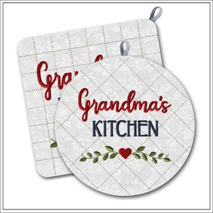 Può includere: Una presina quadrata e una circolare trapuntate in tessuto bianco con un sottile motivo floreale e cuciture a griglia. Entrambe presentano il testo ricamato in rosso "Grandma's" e in blu "KITCHEN" sopra un piccolo cuore rosso e foglie verdi.