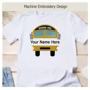 Pode incluir: Uma t-shirt branca com um design de bordado à máquina de um autocarro escolar amarelo no peito. O gráfico do autocarro inclui janelas azuis, o texto SCHOOL BUS e o texto personalizável Your Name Here em letras pretas sob o para-brisas.