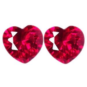 Puede incluir: Dos gemas facetadas en forma de corazón, de un tono rojo vibrante. Las gemas tienen un tallado brillante, con múltiples facetas que reflejan la luz. Las gemas se colocan sobre un fondo blanco.