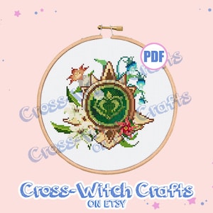 Op de afbeelding: Een kruissteekpatroon met een groen hart omringd door bloemen en bladeren. Het patroon is ingelijst in een houten cirkel en heeft een bruine achtergrond. De tekst "Cross-Witch Crafts on Etsy" staat onderaan de afbeelding.